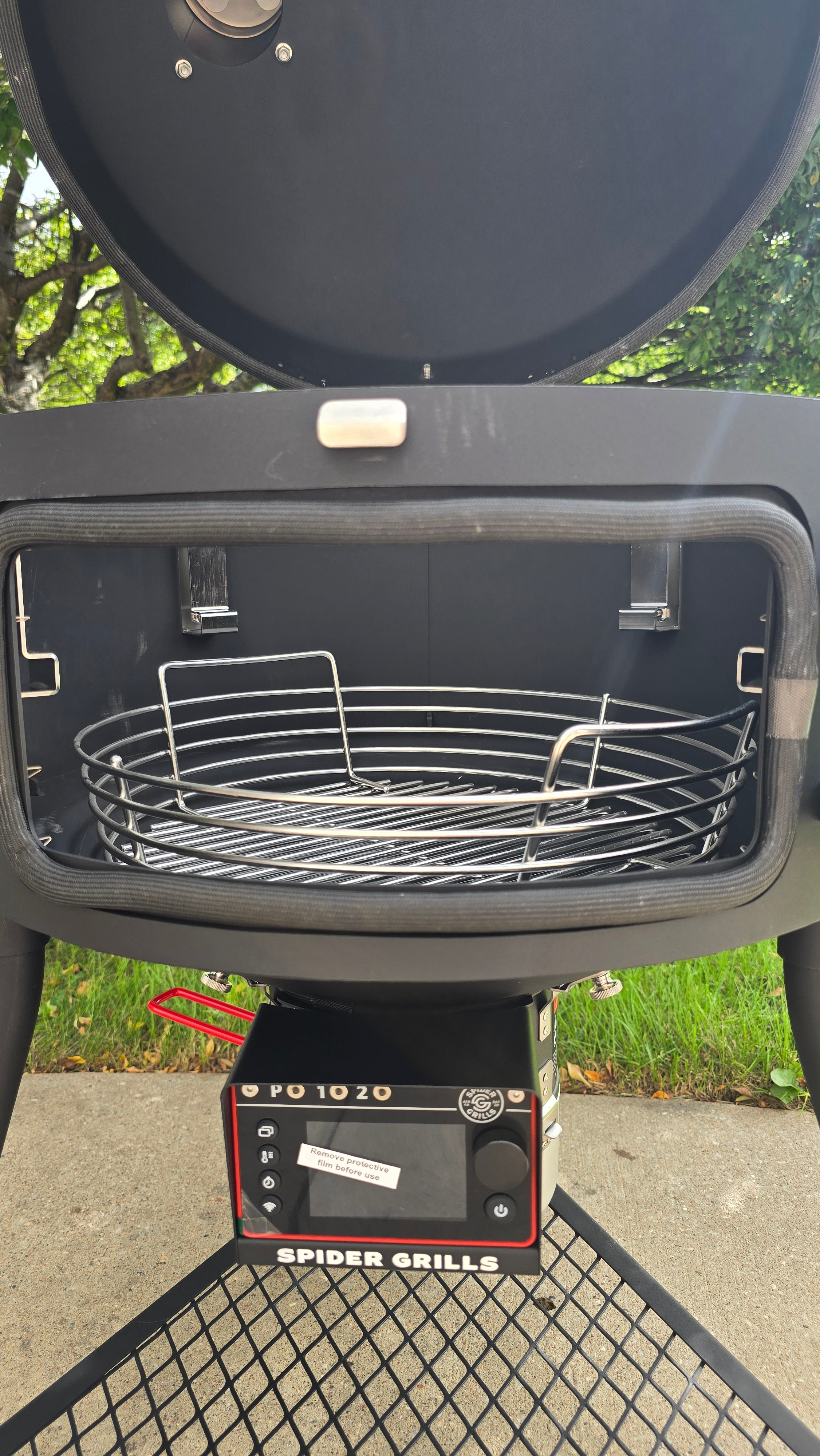 A Spider Huntsman grill with its lid open, showing a 17 inch Kick ash Basket inside. The view is from the side door of the grill.